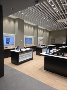 Wide-angle view of a sleek electronics showroom with wall displays, glass display counters, and product tablets on tables under modern ceiling lights.