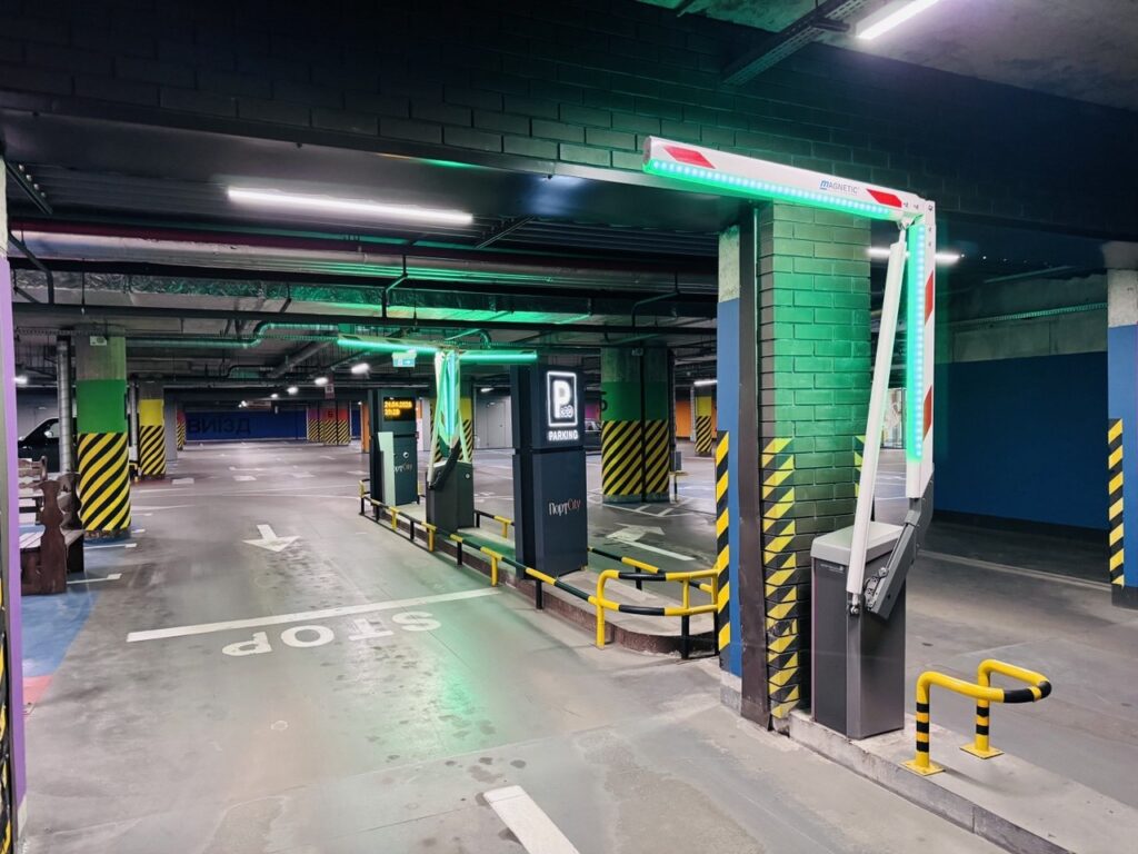 Underground parking entrance with a barrier gate, neon lights, and striped columns.
