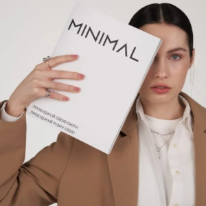 Woman in a beige blazer holds a white magazine titled MINIMAL, partially covering her face.