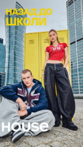 Two young models pose by yellow lockers in a city square with tall glass buildings; large yellow text 'Назад до школи' (Back to school) across the top.